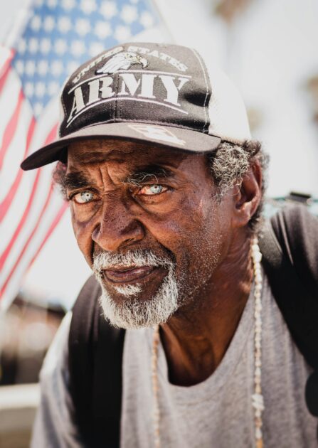 Older U.S. Army veteran with an American flag behind him, representing those eligible for VA Pension and Aid and Attendance benefits.